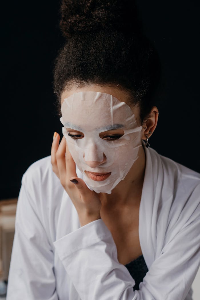 A woman applies a hydrating sheet mask as part of her skincare routine. Indoor setting with a calm ambiance.